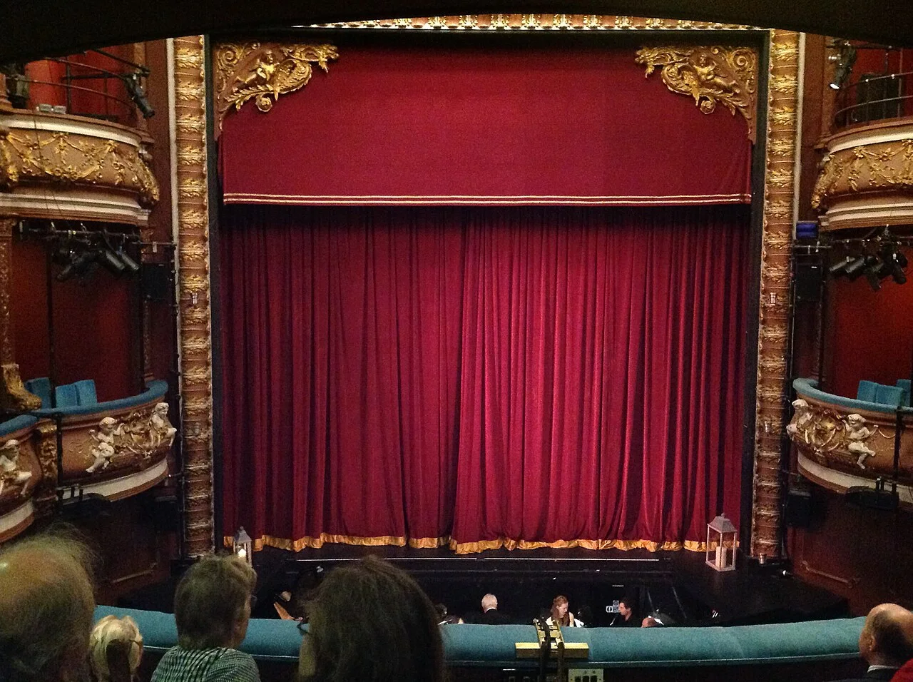 Red theater curtain above an orchestra pit and seats.