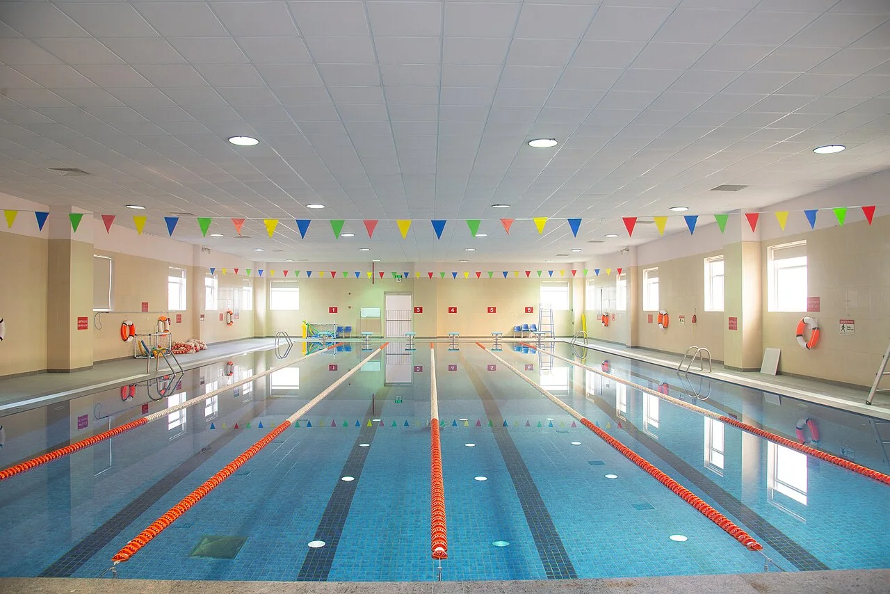 Clear blue indoor swimming pool with orange lane ropes and colorful overhead flags.